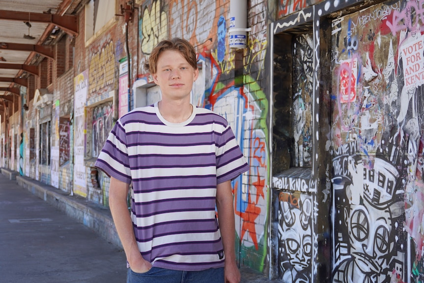 Rowan White in a striped shirt and jeans, holding a skateboard at Fremantle's Woolstores.
