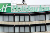 The exterior of a Holiday Inn hotel, with curtains drawn across windows and a green sign.