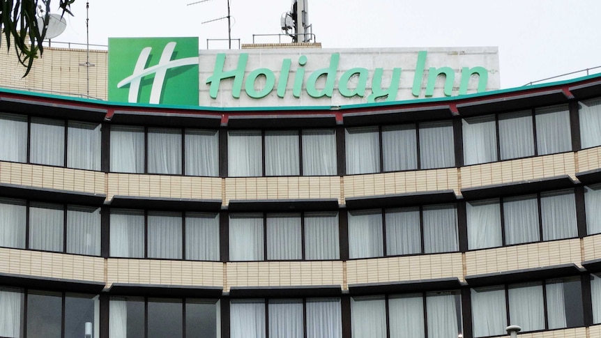 The exterior of a Holiday Inn hotel, with curtains drawn across windows and a green sign.