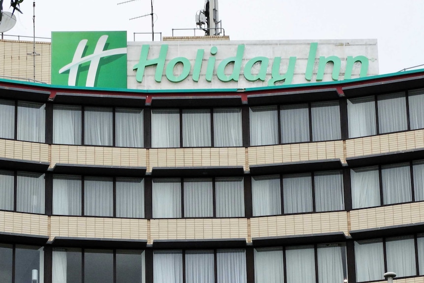 The exterior of a Holiday Inn hotel, with curtains drawn across windows and a green sign.