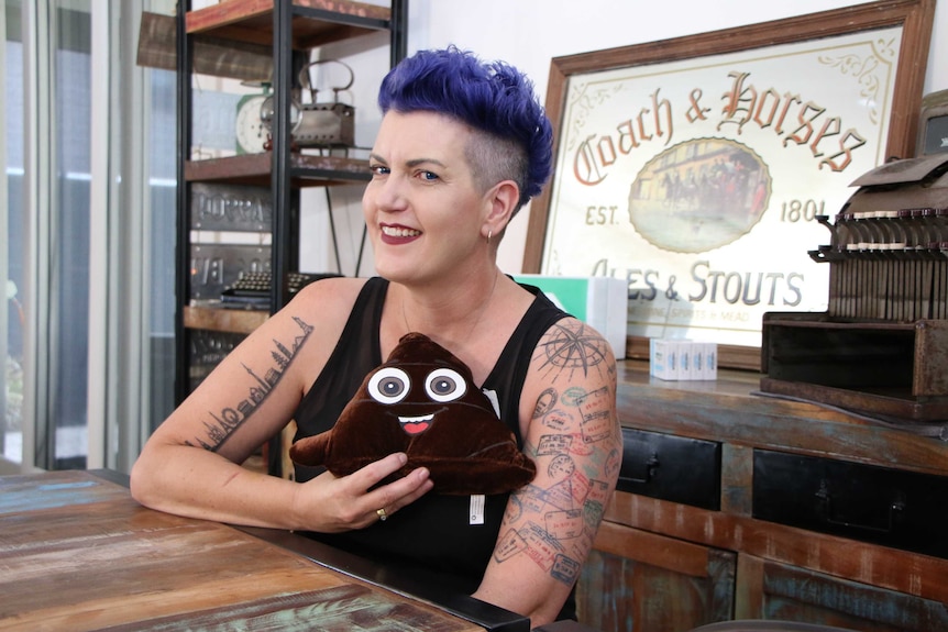 A lady with short purple hair looking at the camera and holding a poo emoji toy
