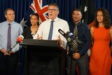 Danial Kelly, Regina McCarthy, Terry Mills, Andrew Bedwell and Amelia Nuku stand at a lectern in front of an Australian flag.