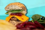 Burger with a seeded bun, spinach, pineapple, beetroot, cheese and patty on a board to depict how to make burgers healthy.