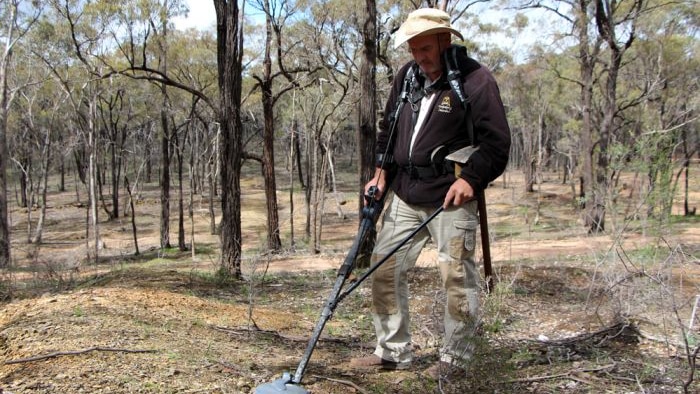 A man looks for gold with a metal detector in the bush