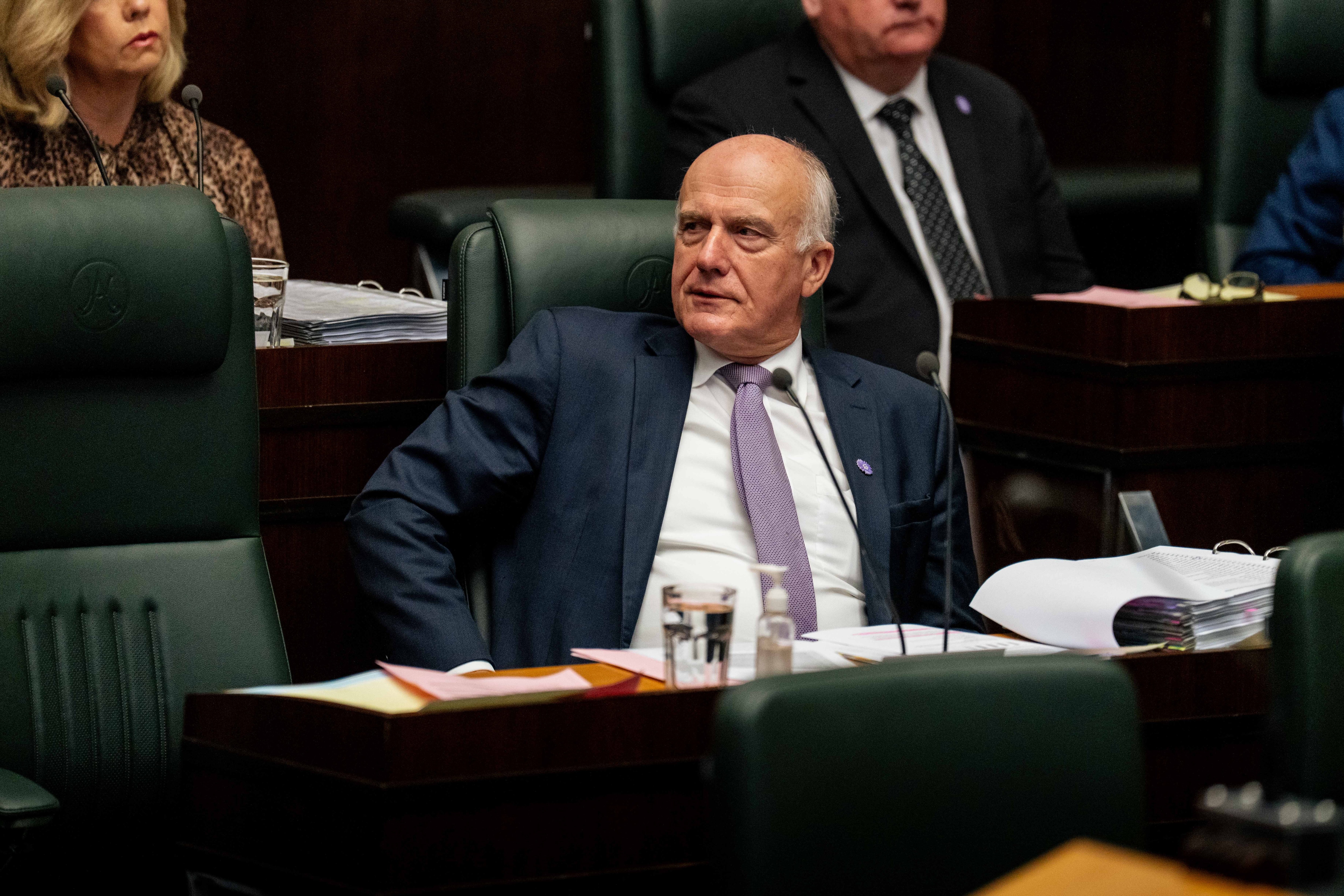 A man dressed formally sits in a green chair in parliament among others