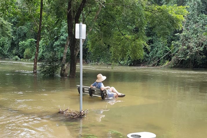 A person sits on a chair in flooded Goomboora Park surrounded by water.