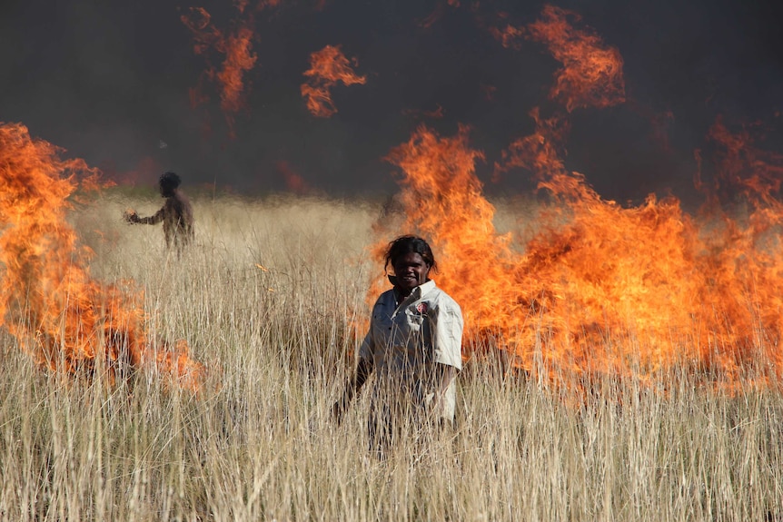 Two Indigenous people in burning dry grass country.
