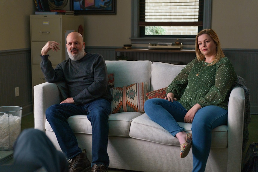 David Cross, a bald white man, and Sarah Steele, a blonde white woman, sit on opposing ends of a therapy couch.