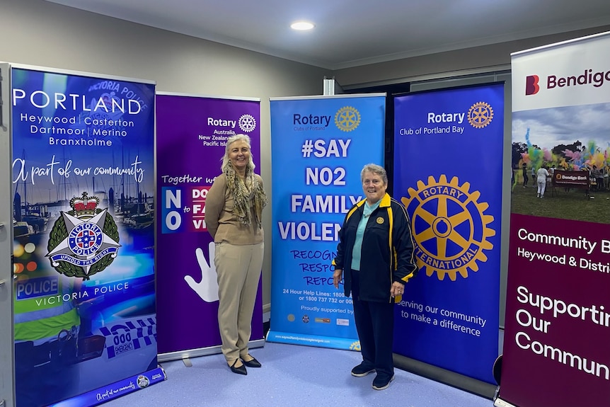 Two women stand in front of banners from Victoria Police Portland, SayNO2family violence, Rotary  and Bendigo Bank 