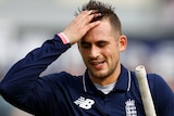 Alex Hales carries a cricket bat, gloves and mask in his hand and runs his hand through his hair with a disappointed expression