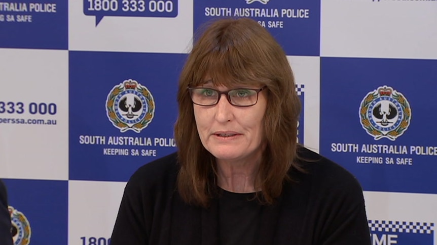 A brunette woman wearing glasses sitting in front of an SA Police background