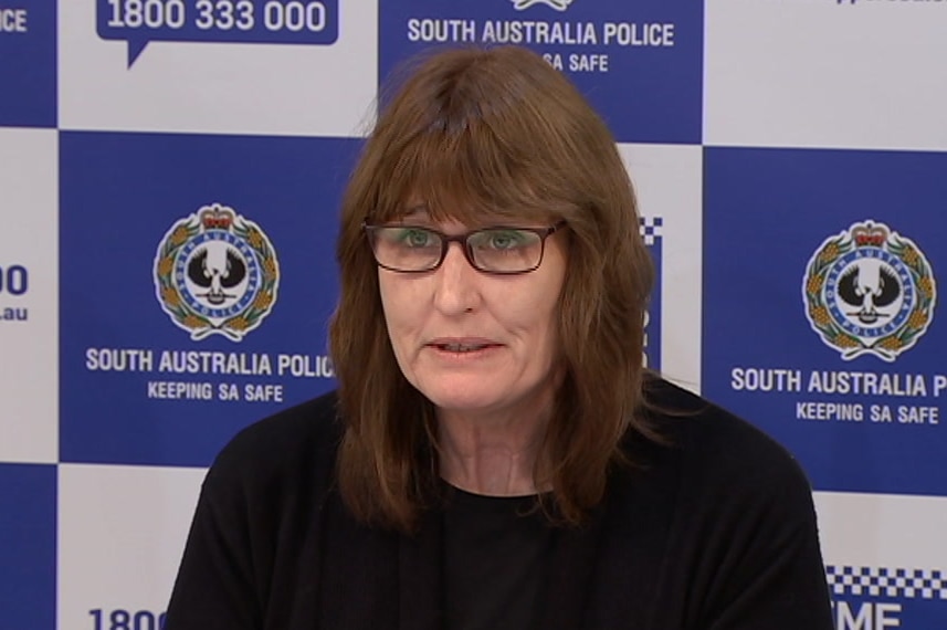 A brunette woman wearing glasses sitting in front of an SA Police background