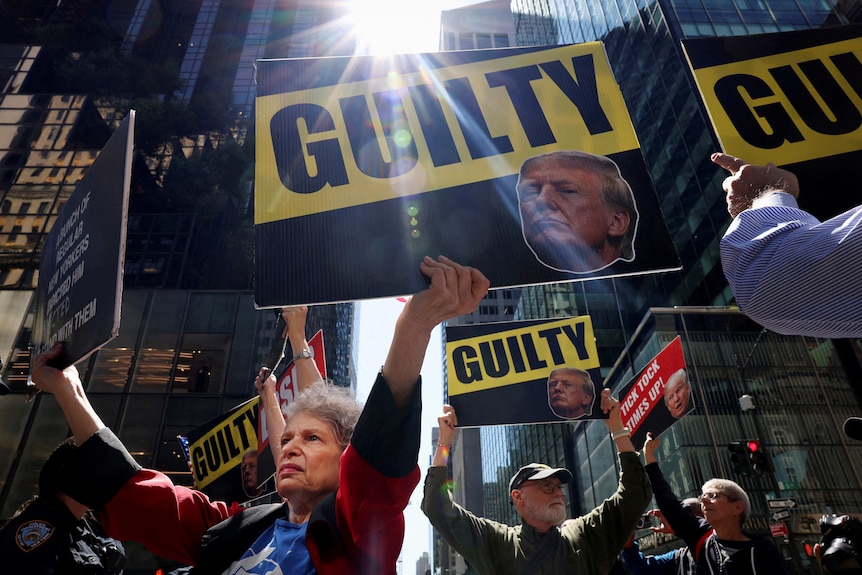 protestors hold signs in the air that read GUILTY outside Trump Tower