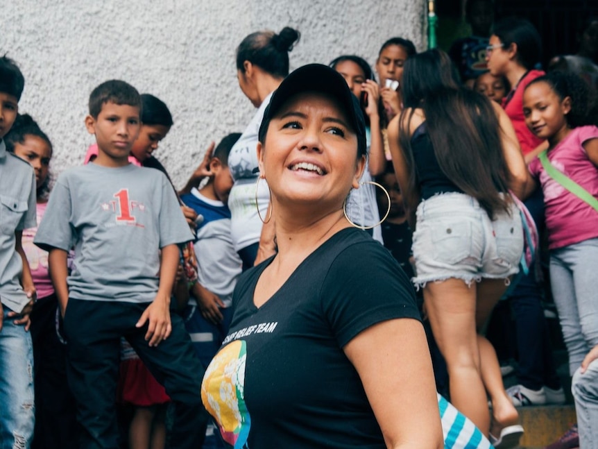 Image of Zomi Frankcom smiling while wearing a cap and a black t-shirt with the WCK logo. Behind her are a lot of kids.