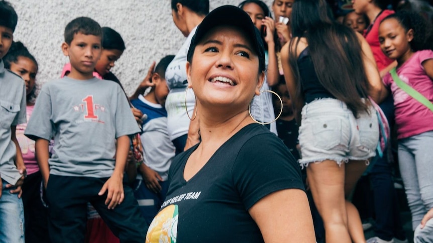 Image of Zomi Frankcom smiling while wearing a cap and a black t-shirt with the WCK logo. Behind her are a lot of kids.