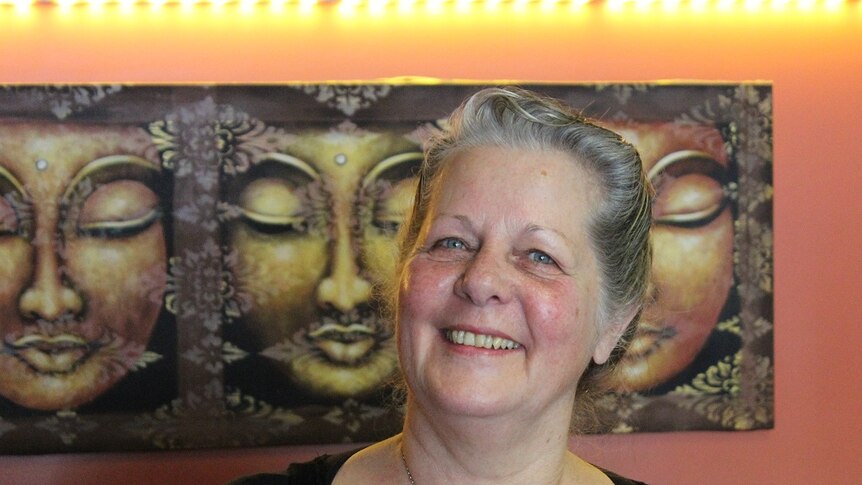 Middle aged woman standing smiling, close up with Balinese artwork in the background.