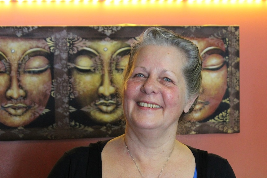 Middle aged woman standing smiling, close up with Balinese artwork in the background.