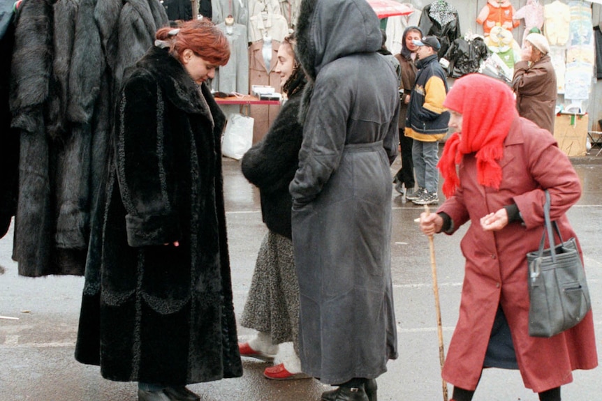 A woman wears a black fur coat surrounded by two women as an elderly woman walks by with a cane.