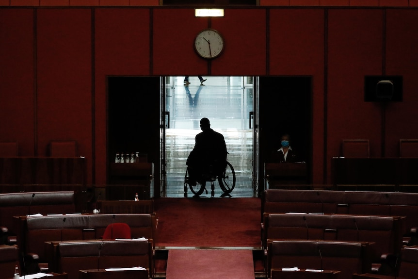 A wide shot of senator jordon steele-john in his wheelchair leaving the senate, he is silouhetted in the doors of the chamber