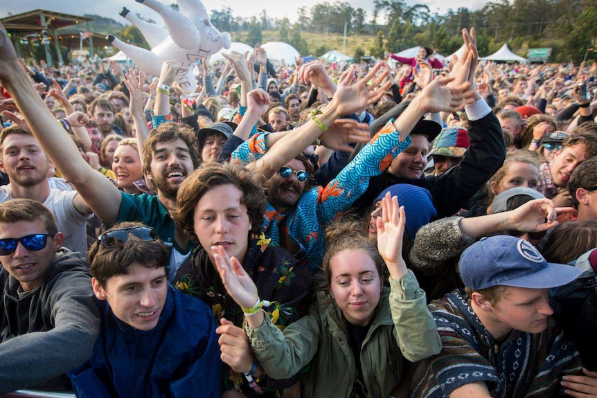 A crowd of young people at a music festival up against the barrier near the stage