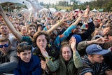 A crowd of young people at a music festival up against the barrier near the stage