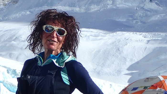 woman in ski goggle and ski suit stands in the snow with a tent in the background.