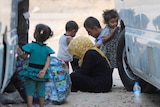 An Iraqi family sits in the dirt between two vans