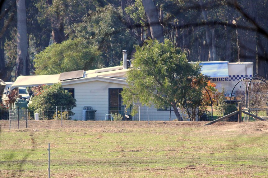 A shack-like home on a rural bush property with a police vehicle behind.