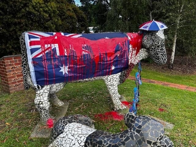 A statue of a cow covered in an Australian flag with red paint thrown over it