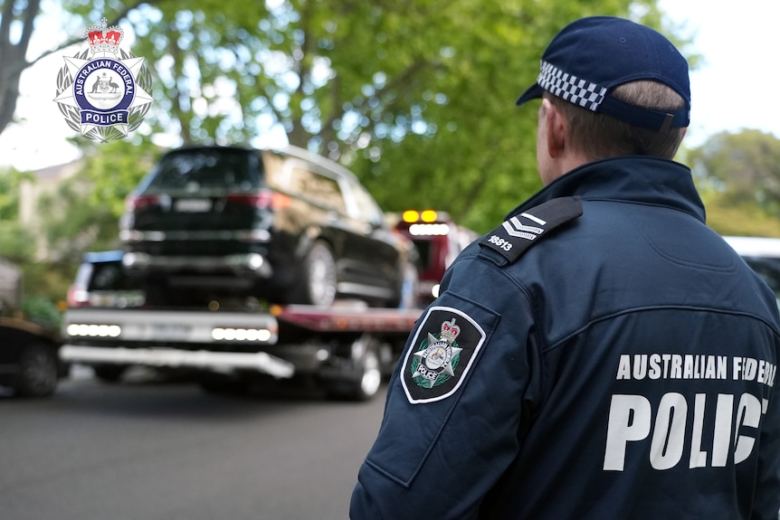 A police officer watches as a luxury car is loaded onto a truck.