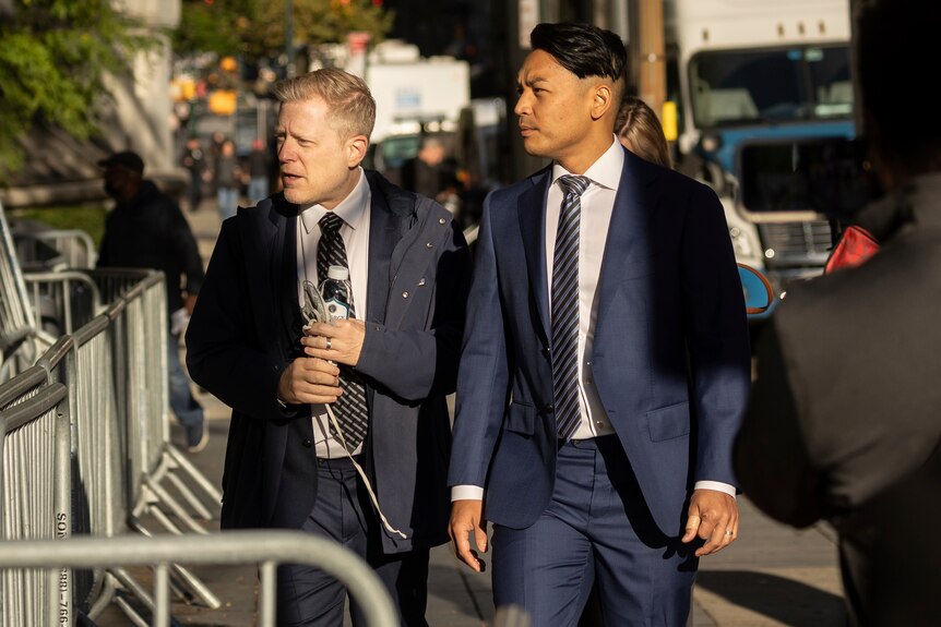 Two men dressed in suits walk on the footpath. 