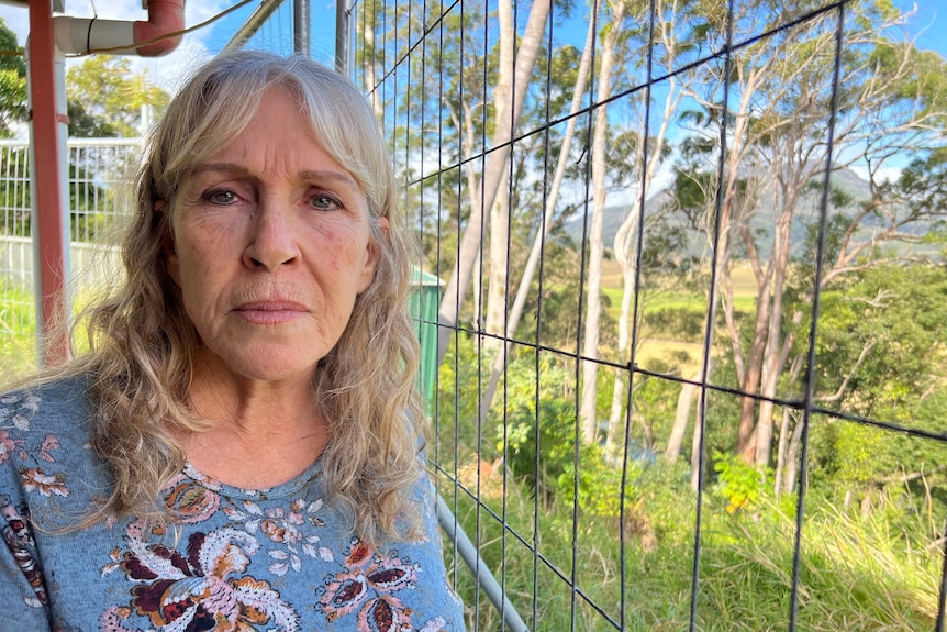 A woman looks at the camera with a sad face as she stands next to a safety fence on her property