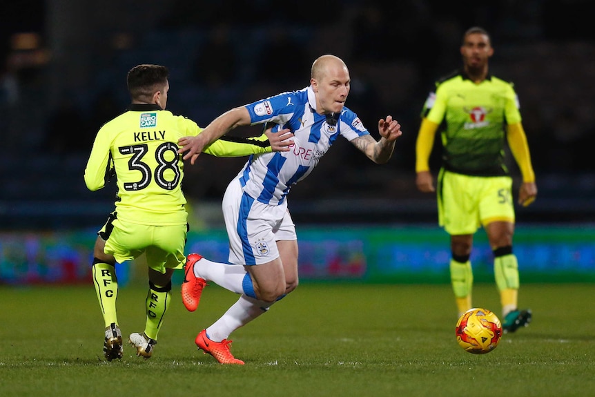 Aaron Mooy turns past a man while playing for Huddersfield Town.