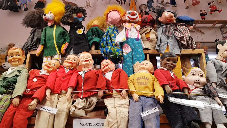 A large number of puppets hang in a collection from the wall.