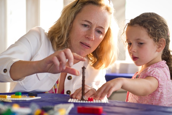 A parent playing with a child and some colourful plastic blocks in a tower