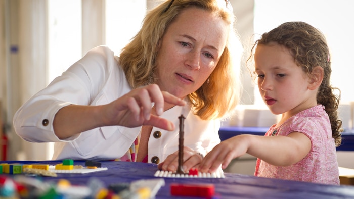 A woman playing with a child and some colourful plastic blocks in a tower