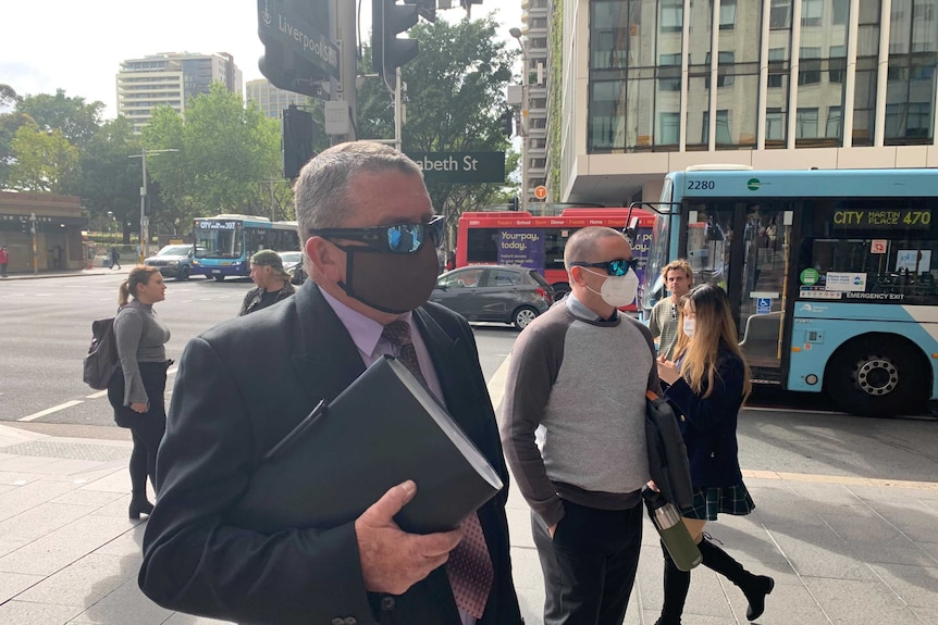 A man in a mask and sunglasses and a suit on a street in Sydney