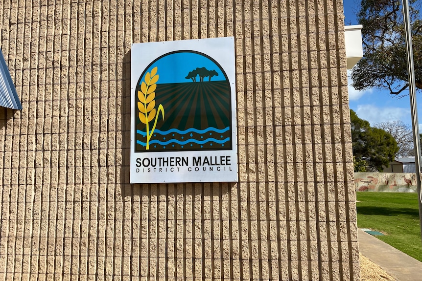 A wall with a sign on it featuring a paddock, water and some wheat. 