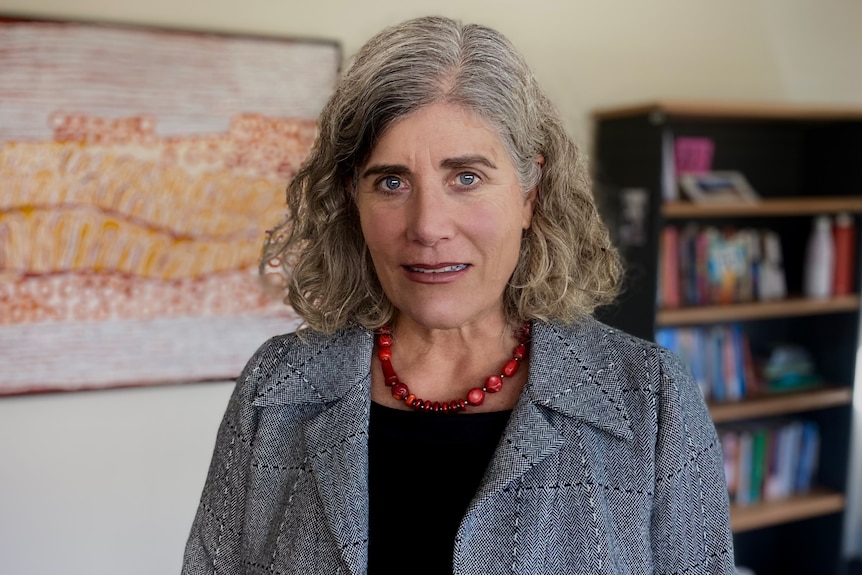 A woman in an office looks into camera with a serious expression.