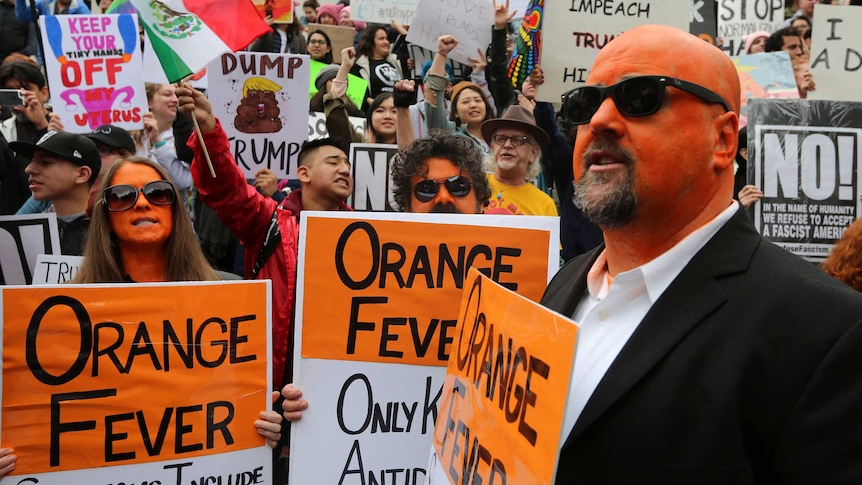 Protesters, some with faces painted orange, rally against US President Donald Trump.
