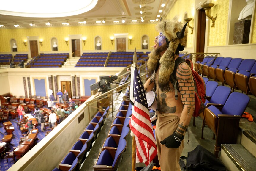 A shirtless, tattooed protester wearing a horned helmet shouts from the upstairs gallery of the US Senate.
