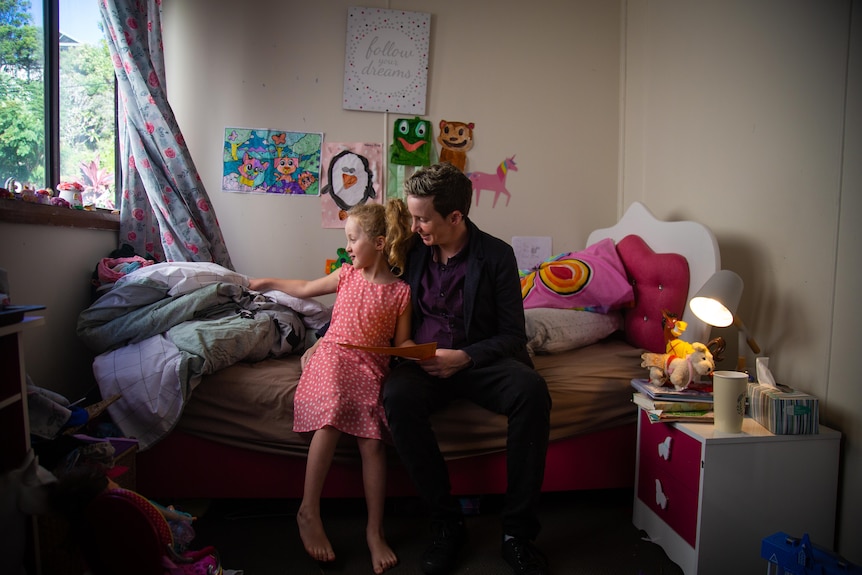 Mother and young daughter sitting together in child's bedroom.