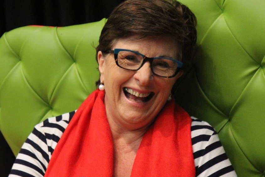 A smiling woman in a black and white striped top and red scarf sits in a green chair.