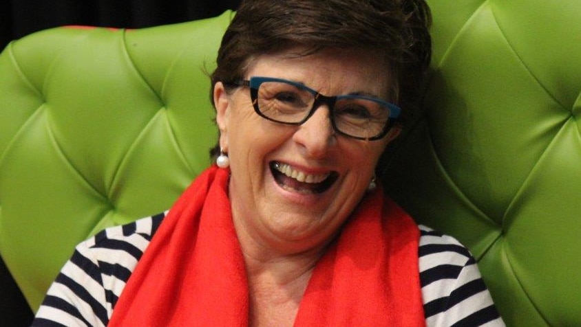 A smiling woman in a black and white striped top and red scarf sits in a green chair.