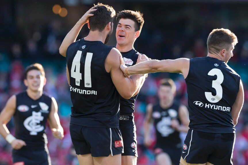 A male AFL player rubs the back of his teammate's head as he smiles in celebrating a goal.