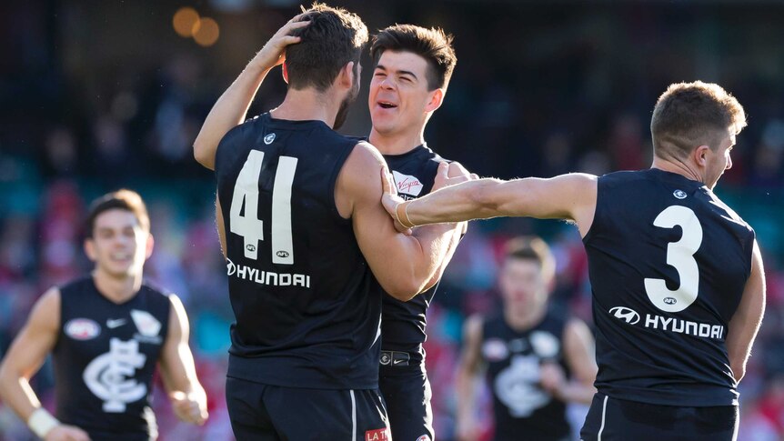 A male AFL player rubs the back of his teammate's head as he smiles in celebrating a goal.