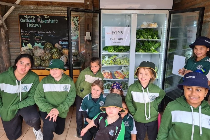 A group of kids wearing green uniforms standing in front of a freezer