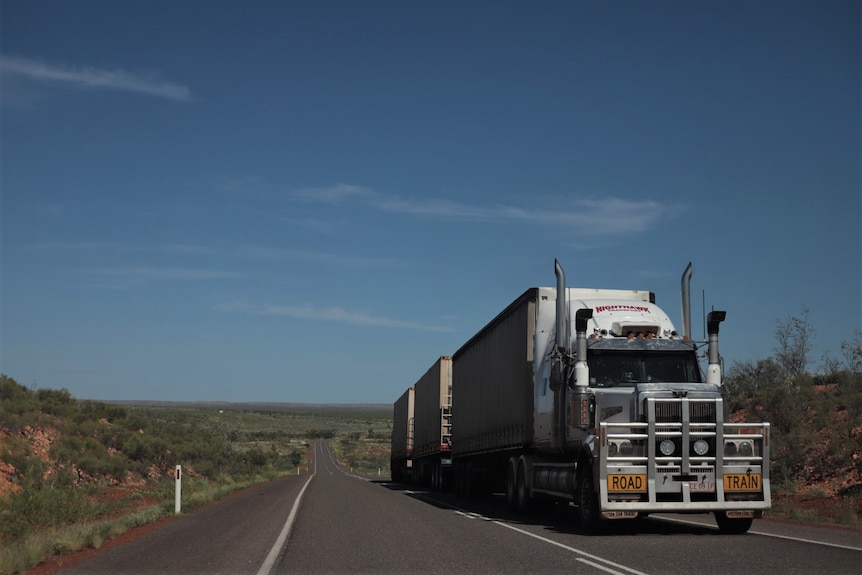 A road train with three trailers drives along an outback highway.