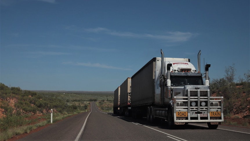 Road train with three trailers drives along outback highway. 