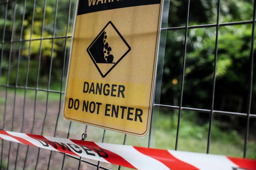 A yellow sign attached to a wire fence with an illustration of falling rocks. The sign reads 'Warning. Danger Do Not Enter'.